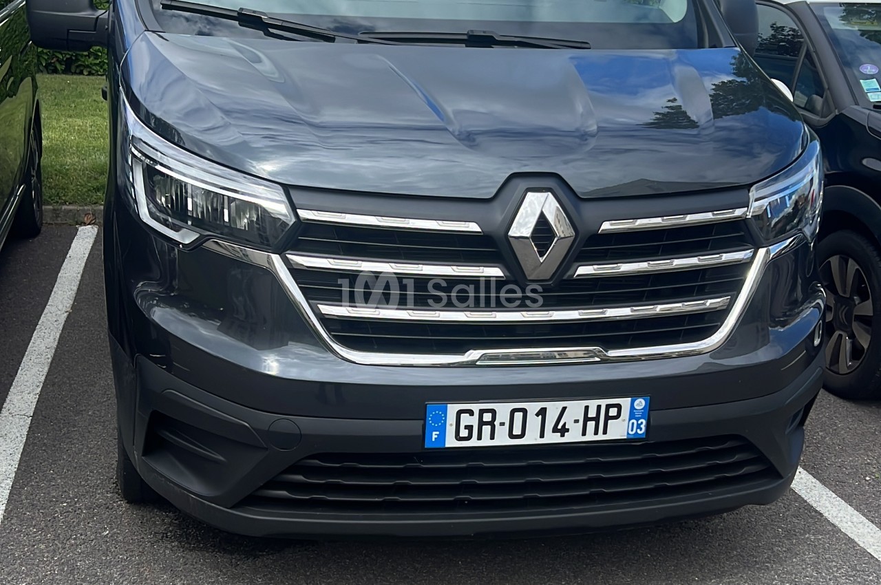 Véhicule utilitaire gris anthracite de marque Renault vu de face, stationné sur un parking goudronné.