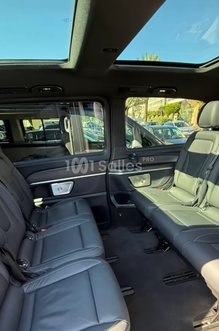 Intérieur d'un van premium aux sièges en cuir noir disposés face à face, avec toit ouvrant panoramique et grandes vitres latérales.