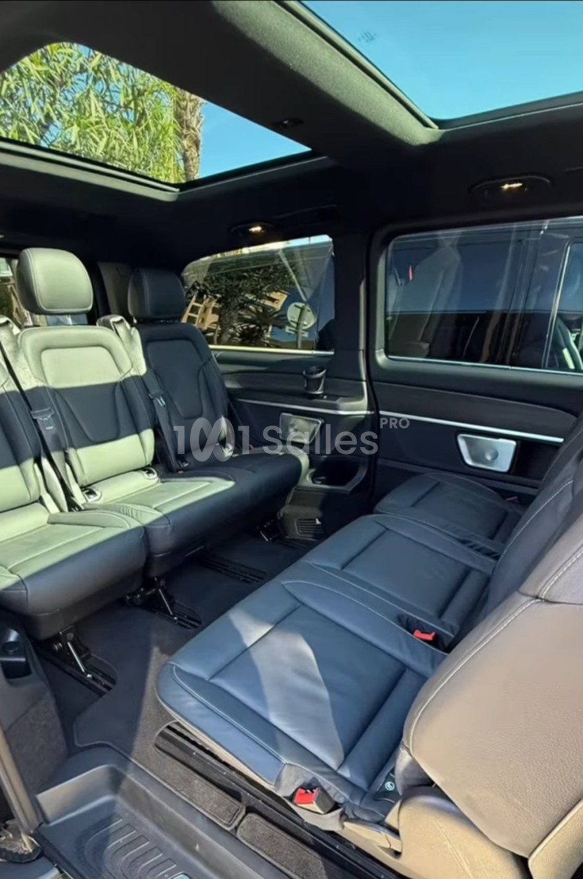 Intérieur d'un van de luxe aux sièges en cuir noir disposés en rangées face à face, avec toit ouvrant panoramique.