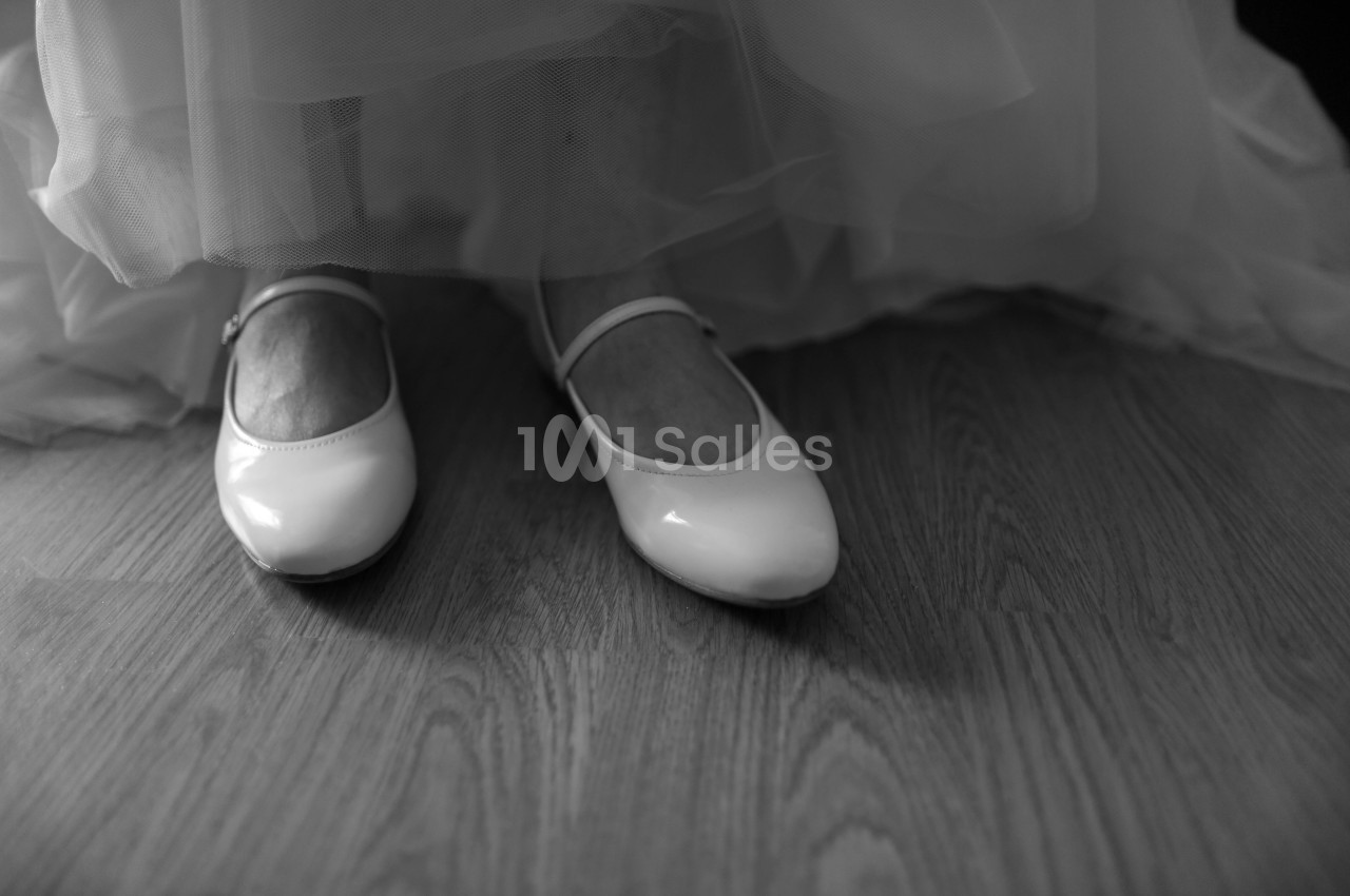 Escarpins vernis blancs à bride, portés sous une jupe de tulle, posés sur un parquet en bois, en noir et blanc.