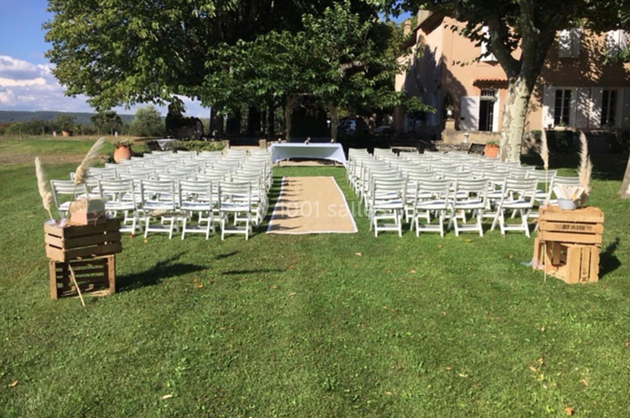 Chaises blanches disposées en rangées sur une pelouse, formant une allée centrale menant à une table décorée en extérieur.