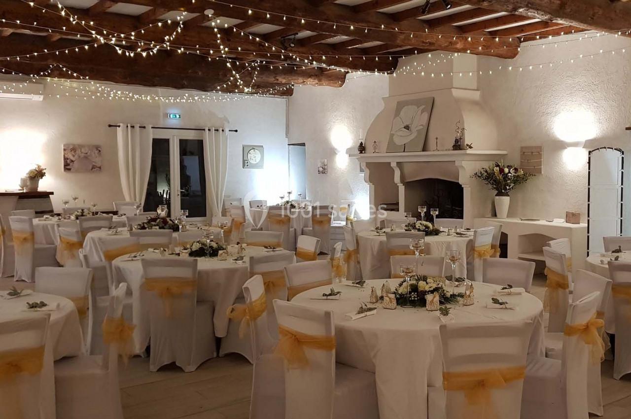 Salle de réception décorée avec des tables rondes, nappes blanches, chaises ornées de nœuds jaunes et guirlandes lumineuses.