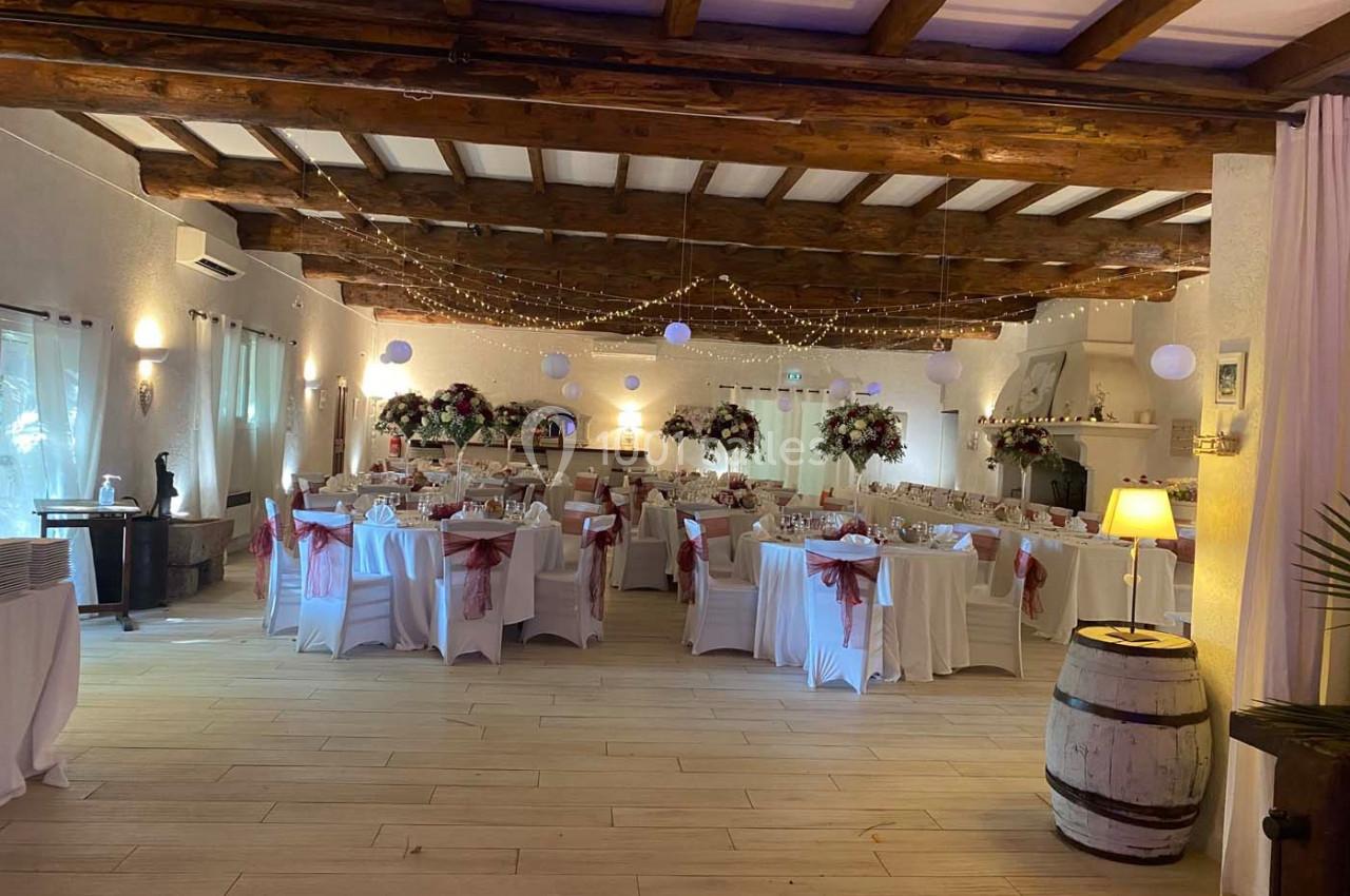 Salle de réception décorée avec des tables dressées, des fleurs, des guirlandes lumineuses et des lanternes suspendues.
