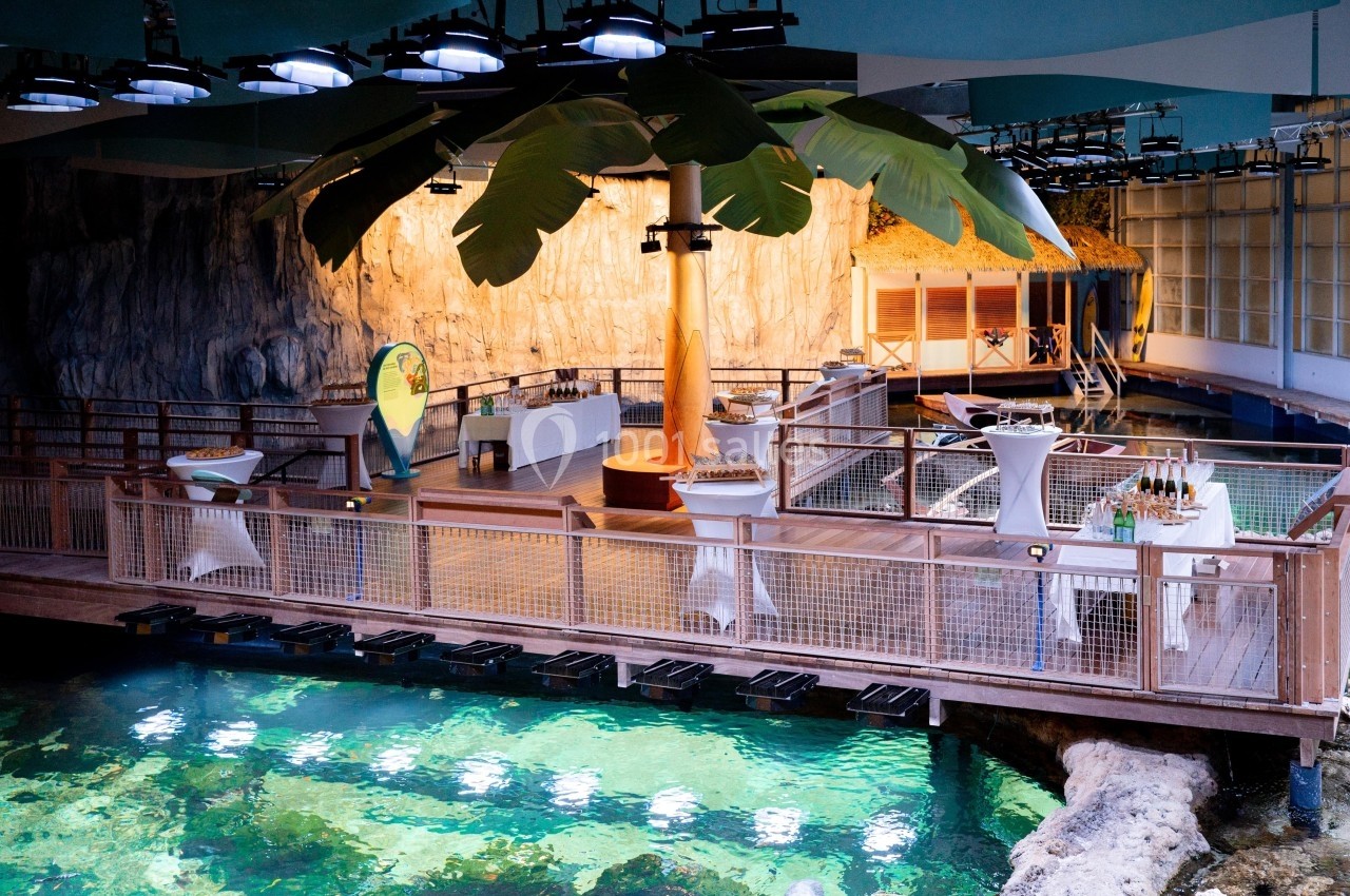 Salle aménagée avec des tables dressées, une passerelle en bois surplombant un bassin d'eau éclairé, et une décoration…