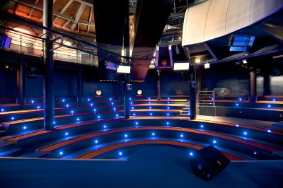 Salle lumineuse avec des tables en bois, des stands d'exposition et des personnes observant ou manipulant des objets.