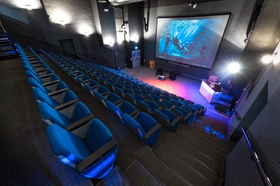 Salle lumineuse avec des tables en bois, des stands d'exposition et des personnes observant ou manipulant des objets.