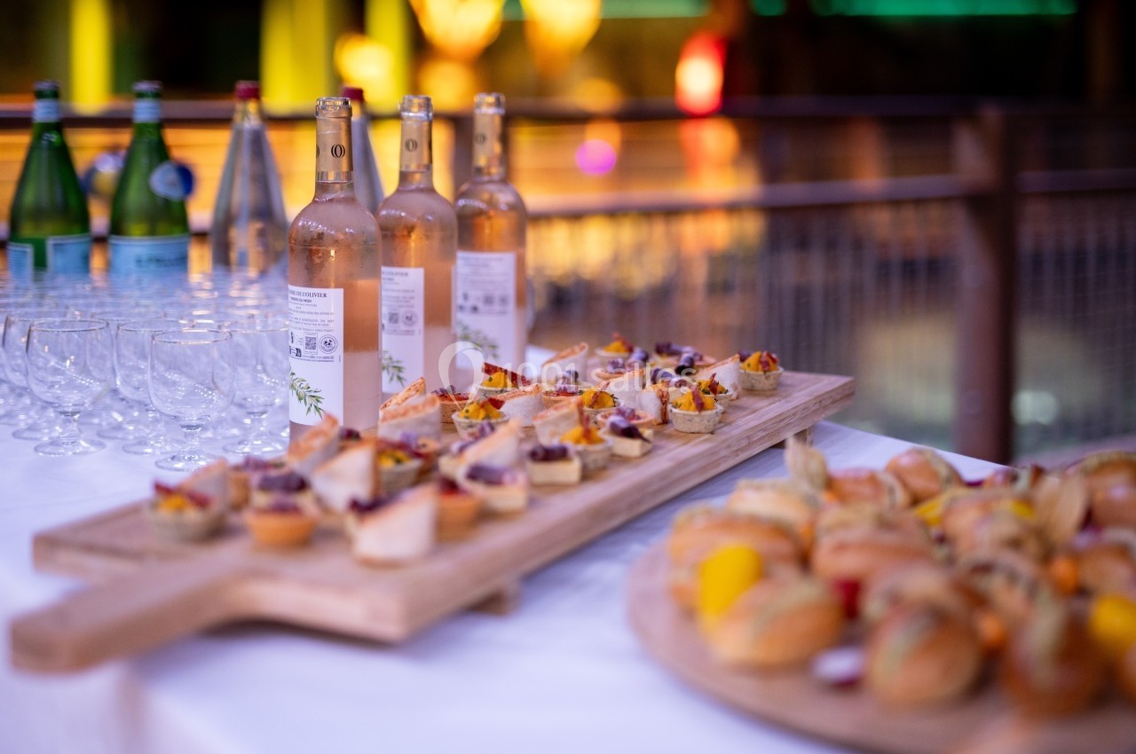 Plateaux de bouchées apéritives variées et bouteilles de vin rosé disposés sur une table avec des verres vides.