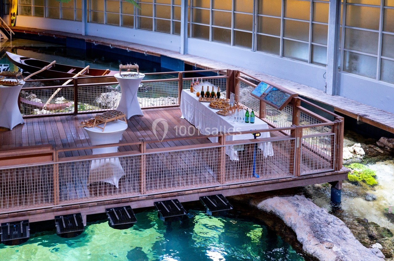 Plateforme en bois surplombant un bassin, aménagée avec des tables dressées pour un buffet.