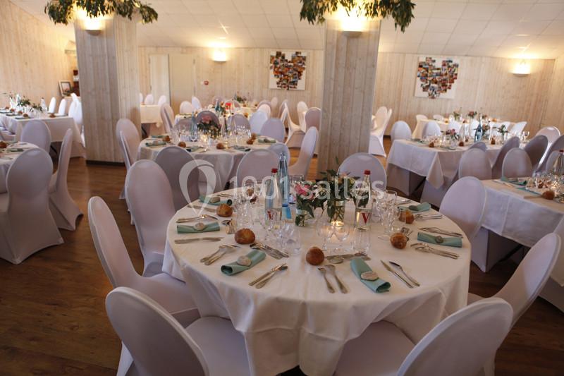 Salle de réception décorée avec des tables rondes dressées, nappes blanches, chaises houssées et centres de table fleuris.
