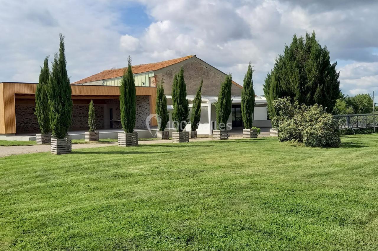 Bâtiment moderne avec façade en bois, entouré de cyprès alignés et d'une pelouse bien entretenue sous un ciel partiellement…