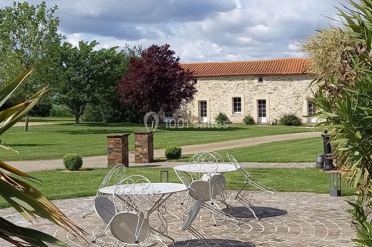 Mobilier de jardin en métal blanc sur une terrasse pavée, avec pelouse, arbres et bâtiment en pierre en arrière-plan.