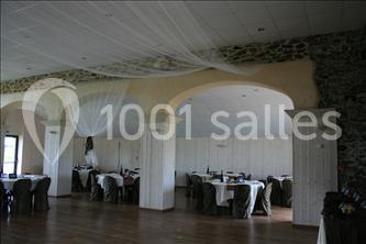 Salle de réception avec tables rondes dressées, murs en pierre et voilages suspendus au plafond.