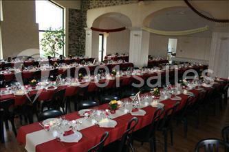 Salle de réception avec de longues tables dressées, nappes rouges, chaises noires et décoration sobre.