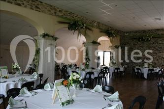 Salle de réception décorée avec des tables rondes dressées, des chaises noires et des arrangements floraux.