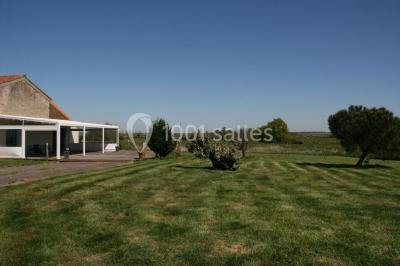 Terrasse en bois avec garde-corps métallique, offrant une vue dégagée sur un paysage champêtre sous un ciel bleu.