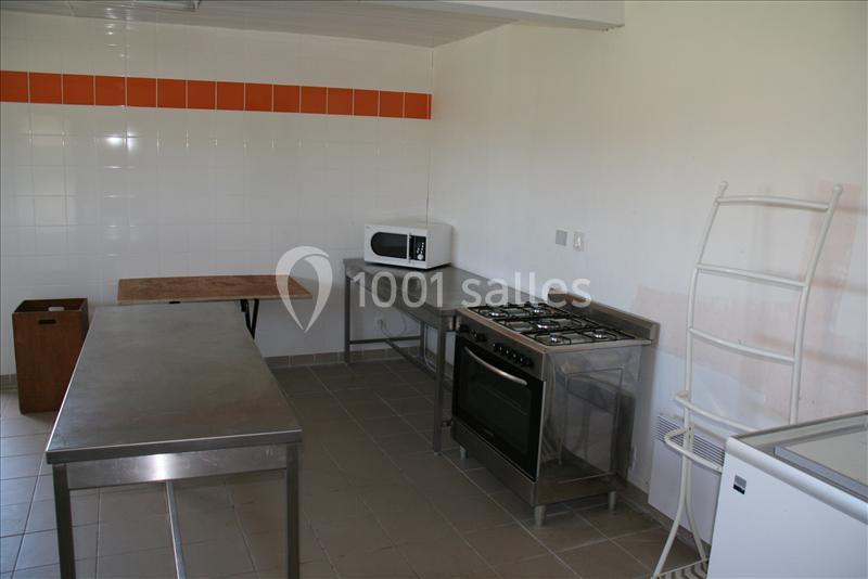 Cuisine simple avec plan de travail en inox, four, micro-ondes, étagère et carrelage mural blanc avec bande orange.