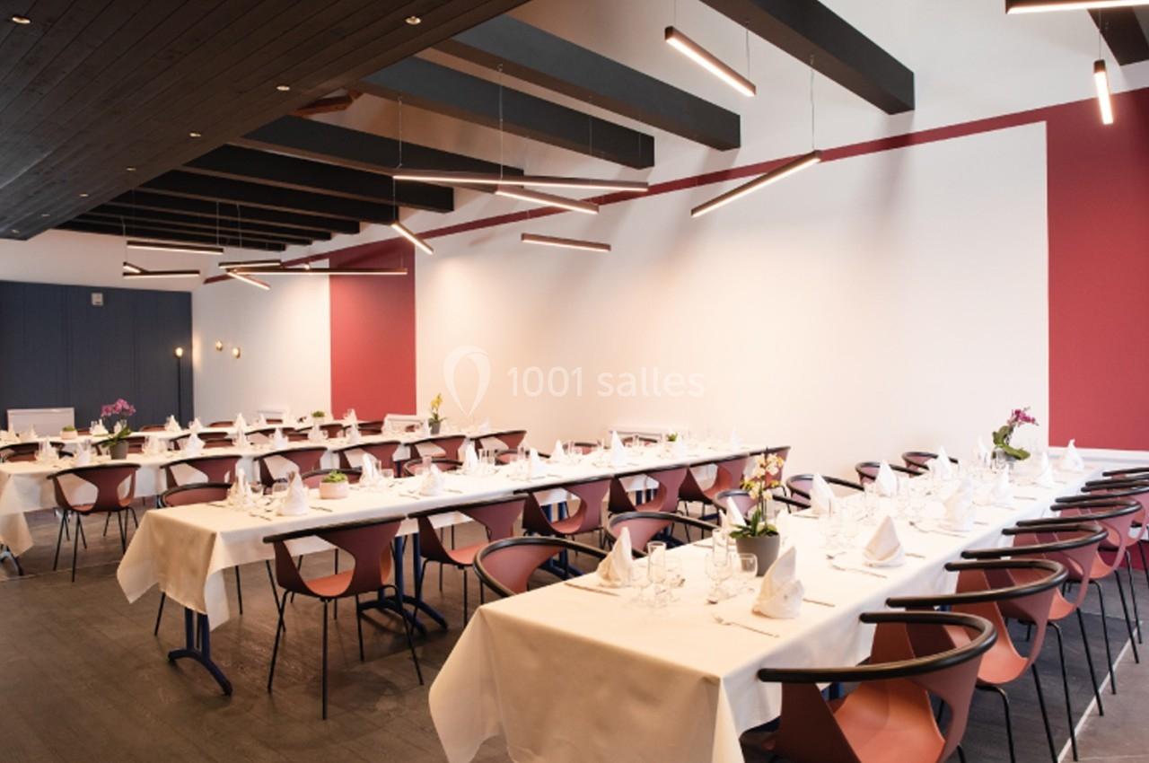 Salle de restaurant moderne avec tables dressées, nappes blanches, chaises design et éclairage suspendu.