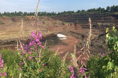 Vue d'une carrière avec des fleurs violettes au premier plan et une petite structure blanche en arrière-plan.