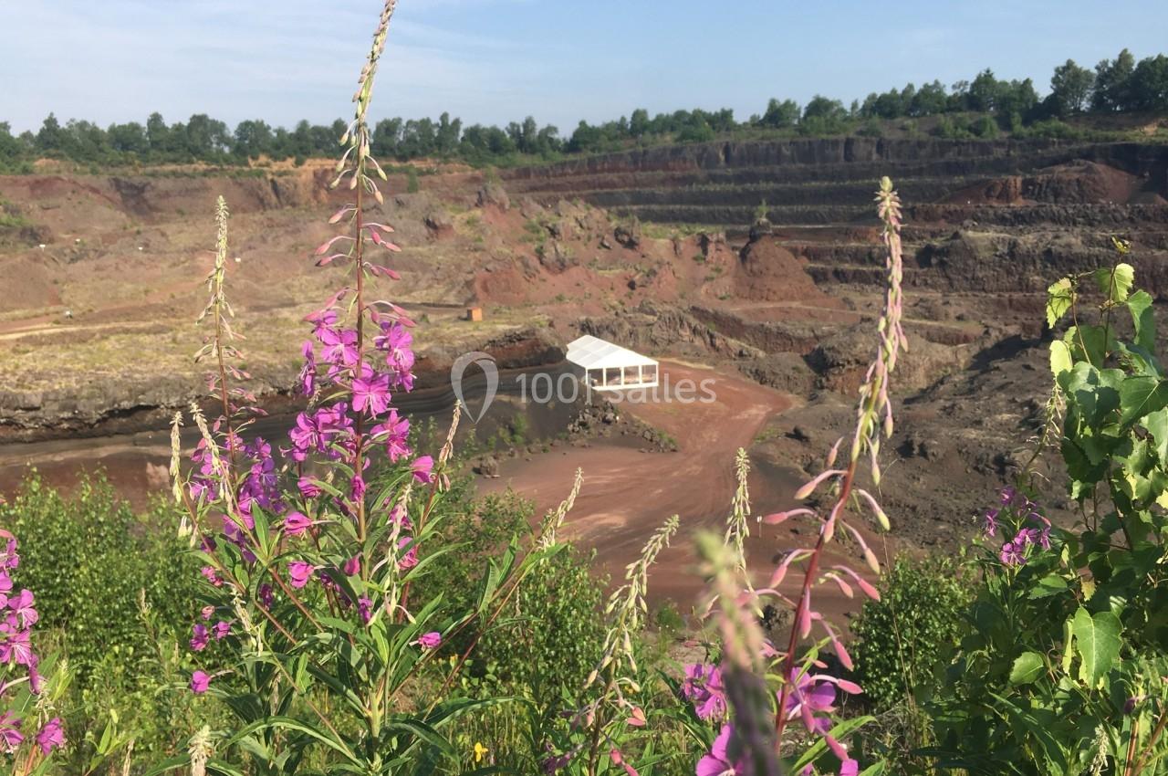 Vue d'une carrière avec des fleurs violettes au premier plan et une petite structure blanche en arrière-plan.
