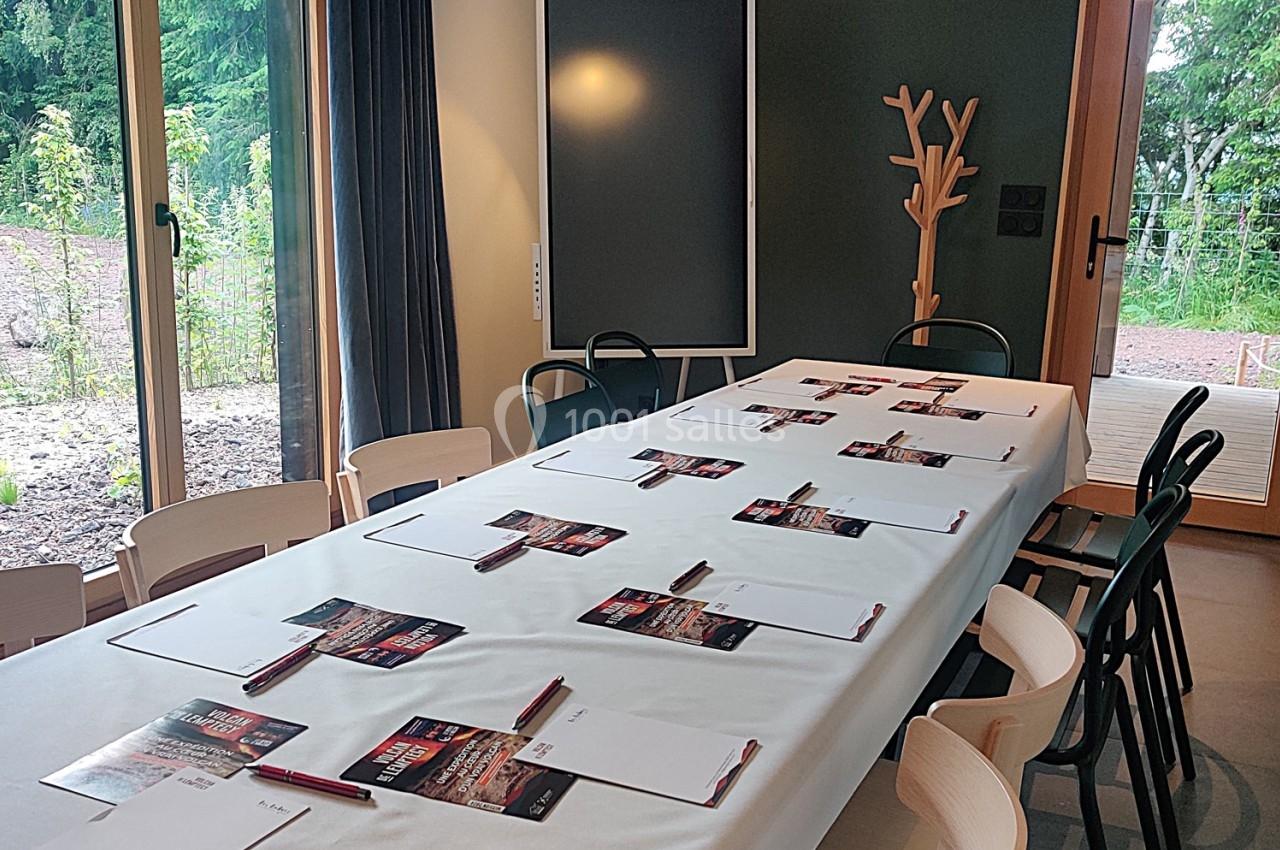 Salle de réunion lumineuse avec une grande table rectangulaire dressée de blocs-notes, stylos et brochures.