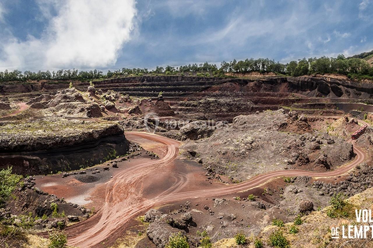 Vue d'un ancien cratère volcanique avec des formations rocheuses rouges et des sentiers sinueux entourés de végétation.