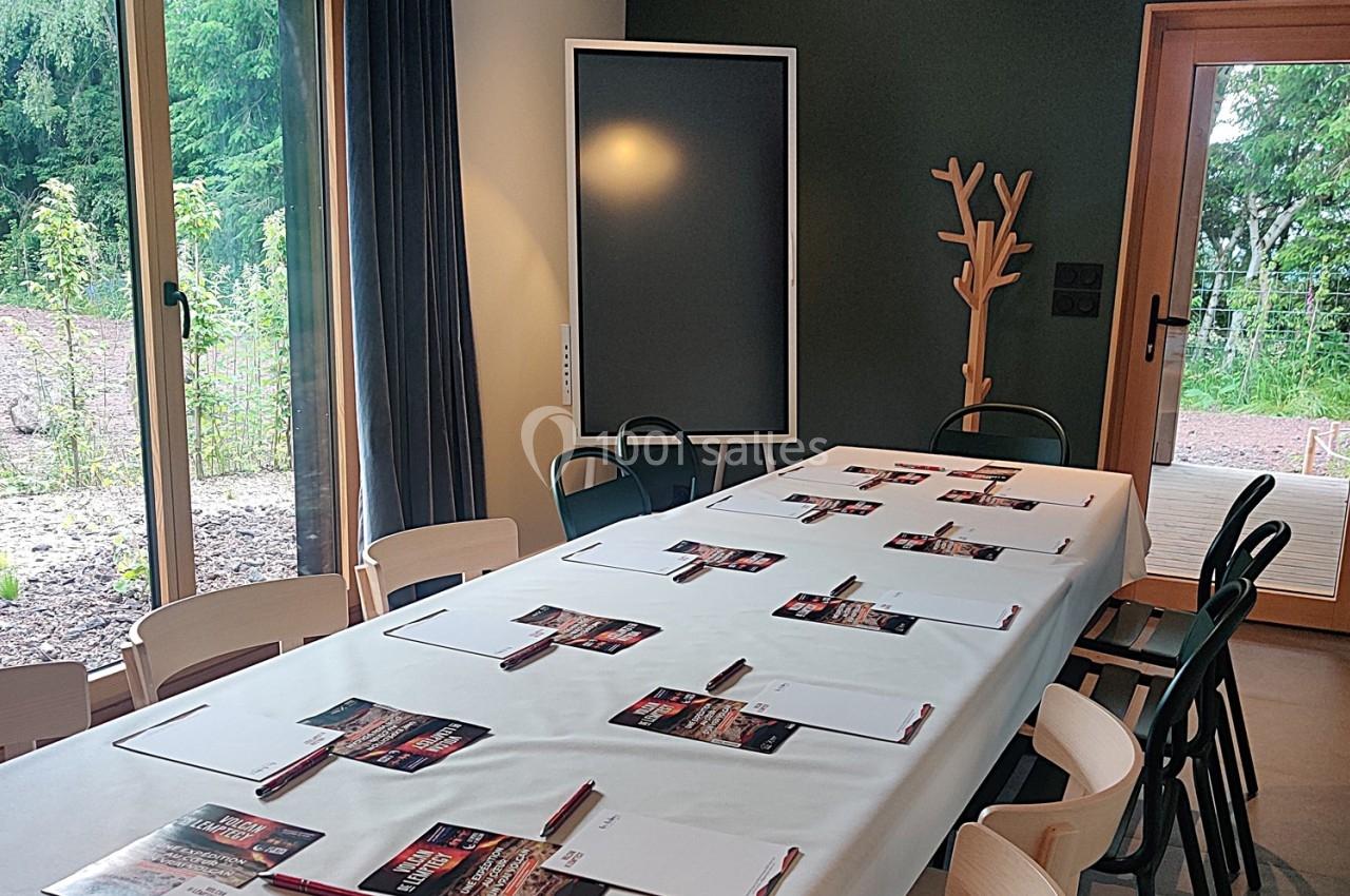 Salle de réunion lumineuse avec une grande table rectangulaire, des chaises, des blocs-notes et des stylos disposés.