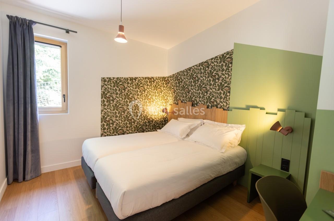 Chambre lumineuse avec lit double, mur décoré de papier peint à motifs végétaux et éclairage d'appoint.