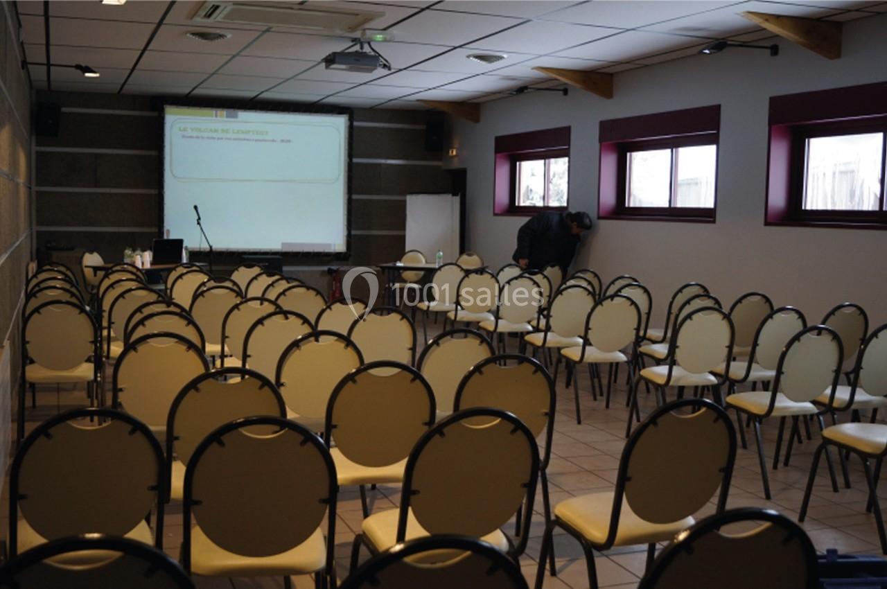Salle de conférence vide avec des chaises alignées, un projecteur allumé et une personne ajustant un équipement.