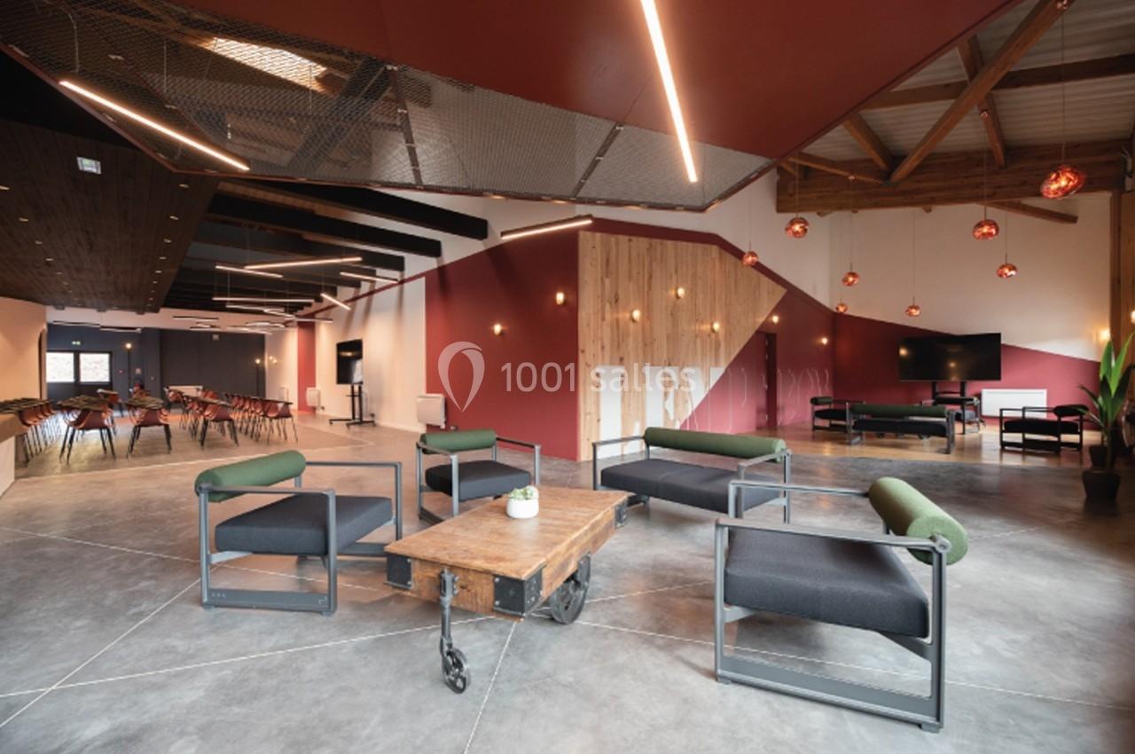 Espace intérieur moderne avec fauteuils, table basse en bois, éclairage suspendu et murs aux tons rouges et bois.