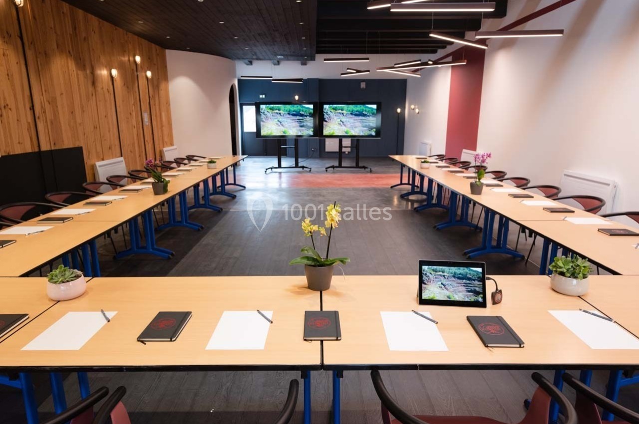 Salle de réunion en configuration en U avec tables, chaises, écrans, plantes et matériel de prise de notes.