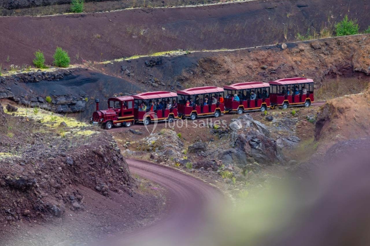 Petit train touristique rouge transportant des passagers sur un chemin sinueux dans un paysage volcanique.
