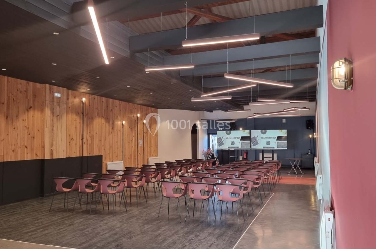 Salle de conférence moderne avec des chaises alignées, un écran de projection et un éclairage suspendu.