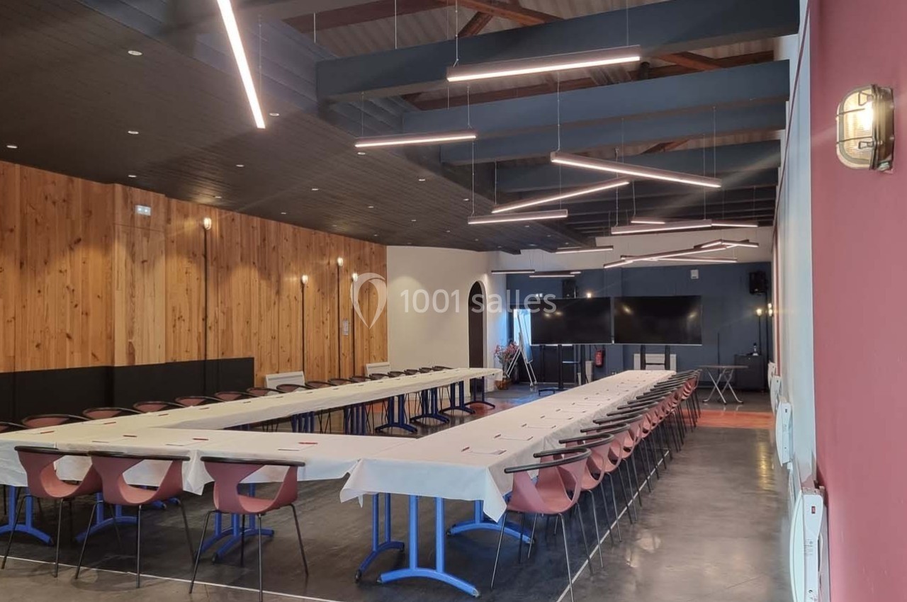 Salle de réunion spacieuse avec de longues tables disposées en U, éclairage moderne et murs en bois et rouge.
