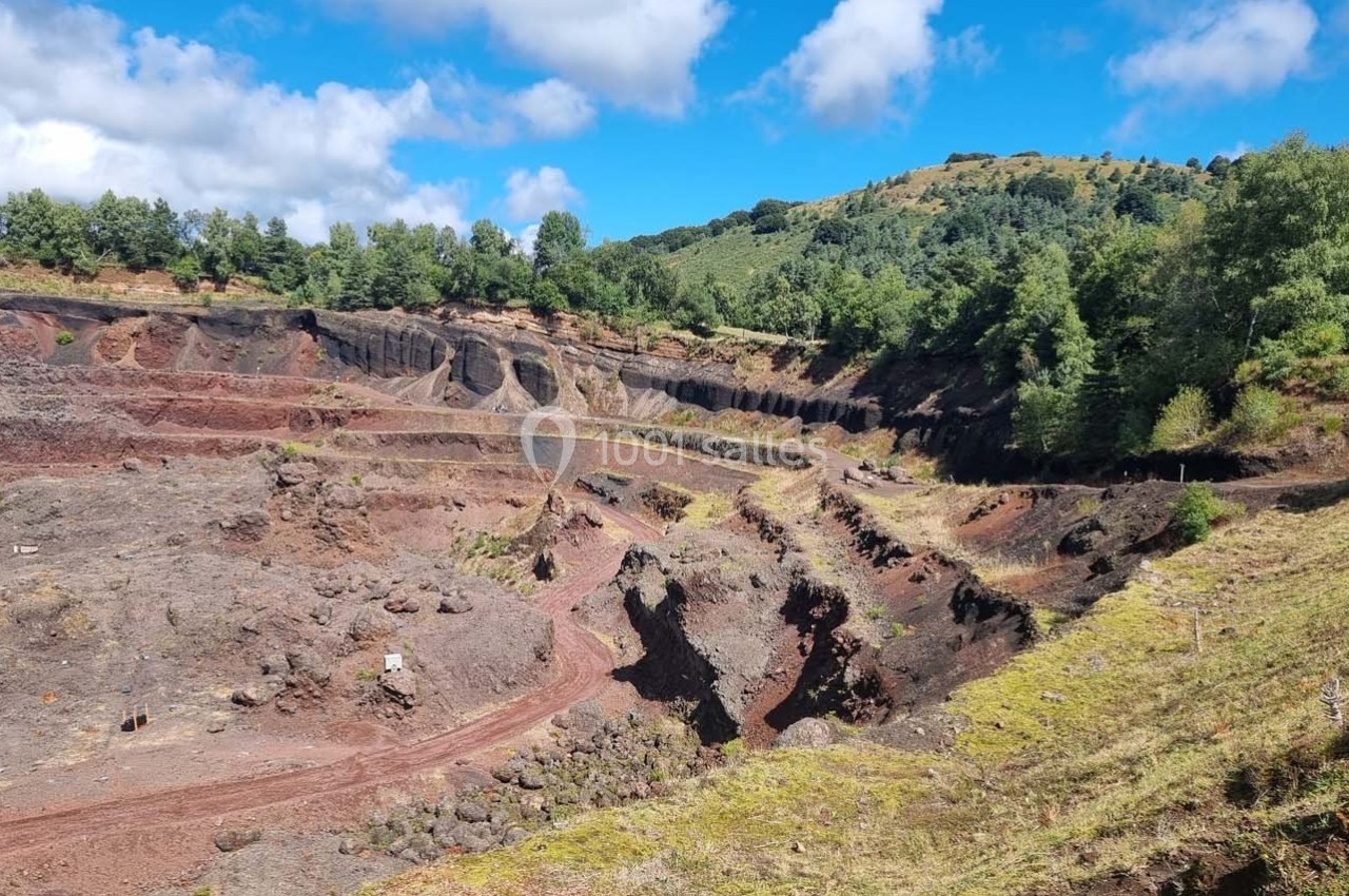 Paysage d'une ancienne carrière volcanique entourée de végétation et de collines sous un ciel partiellement nuageux.