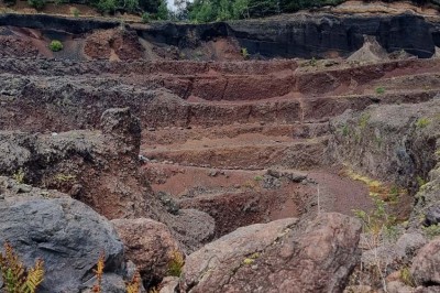 Paysage d'une ancienne carrière volcanique avec des formations rocheuses, entourée de végétation et sous un ciel bleu.