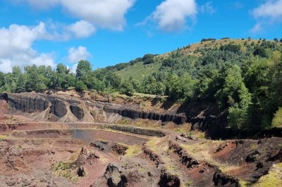 Paysage d'une ancienne carrière volcanique avec des formations rocheuses, entourée de végétation et sous un ciel bleu.