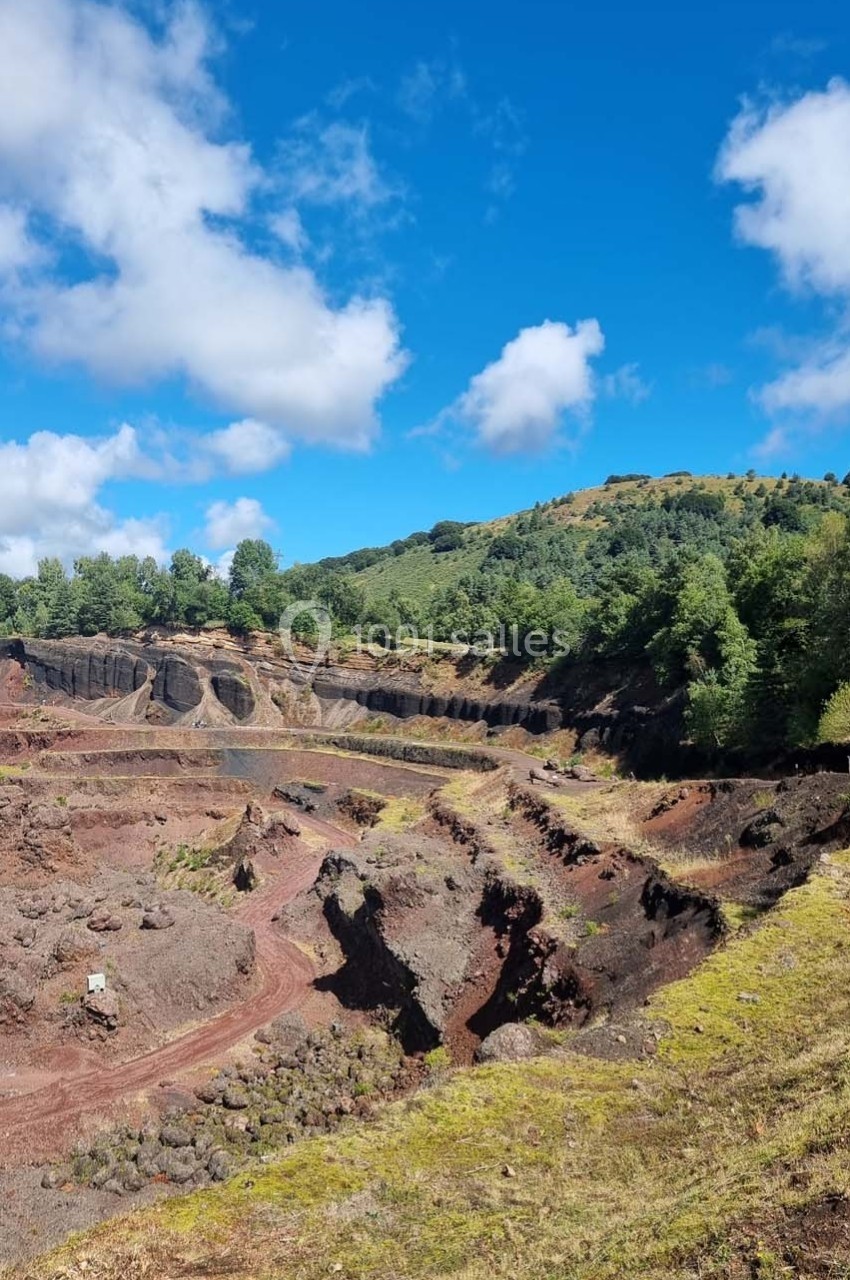 Paysage d'une ancienne carrière volcanique avec des formations rocheuses, entourée de végétation et sous un ciel bleu.