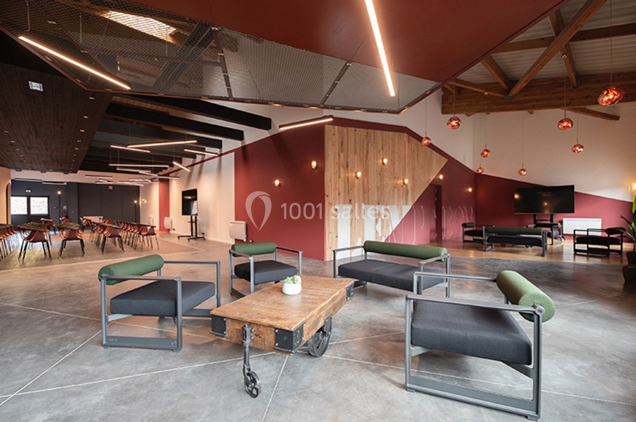 Espace intérieur moderne avec fauteuils, table basse en bois, éclairage suspendu et coin salle de réunion en arrière-plan.