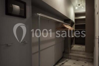 Couloir étroit avec sol en marbre, portant métallique, cintres en bois et étagères au fond sous un éclairage tamisé.