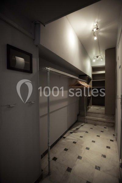 Couloir étroit avec sol en marbre, portant métallique, cintres en bois et étagères au fond sous un éclairage tamisé.