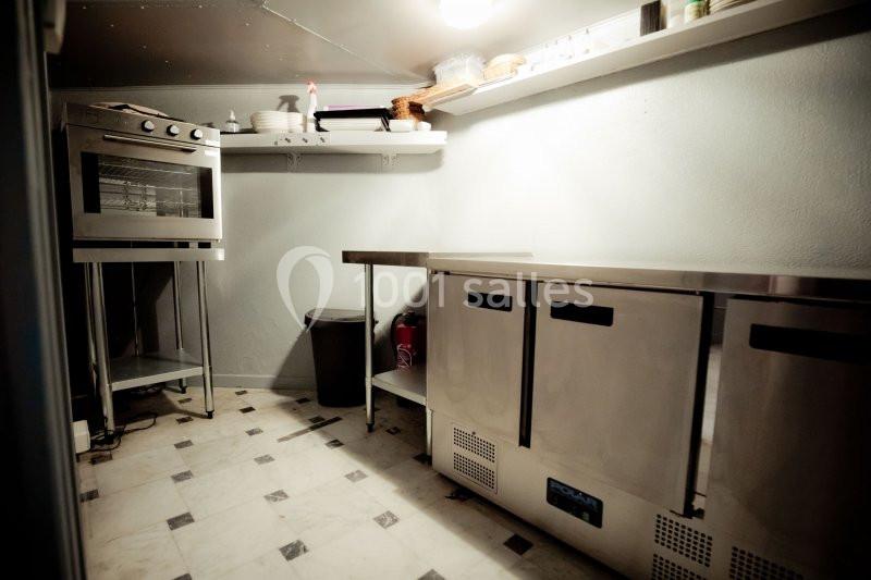 Cuisine professionnelle avec four, étagères, plans de travail en inox et sol carrelé.