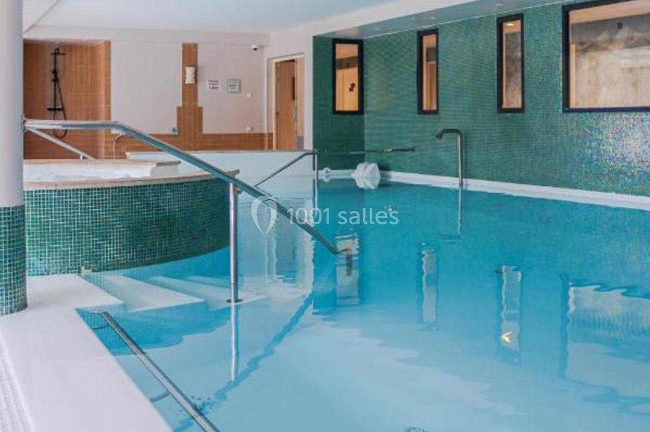 Piscine intérieure avec eau claire, carrelage vert, rampes d'accès métalliques et espace spa en arrière-plan.