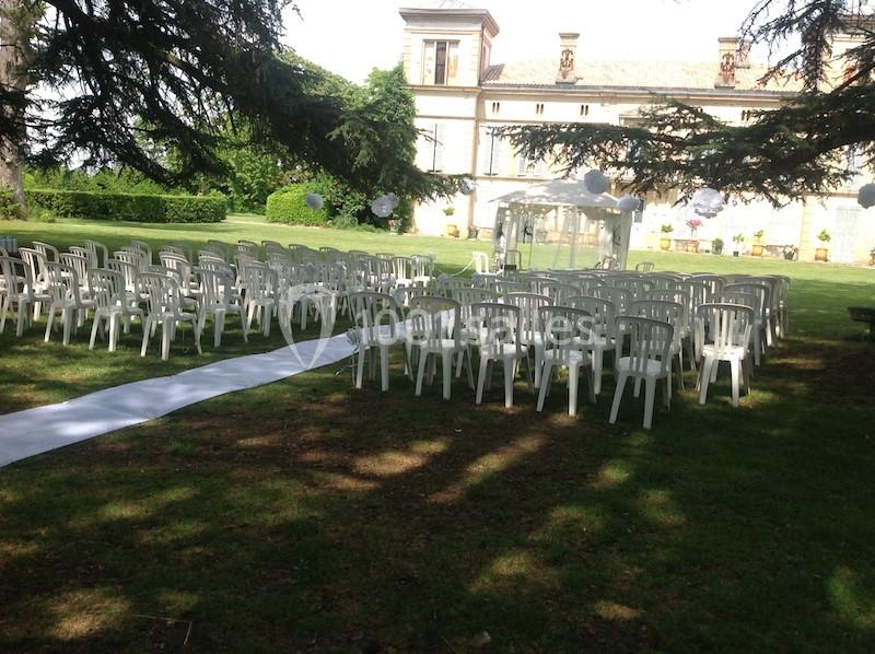 Chaises blanches disposées en rangées sur une pelouse, avec une allée centrale et un bâtiment en arrière-plan.