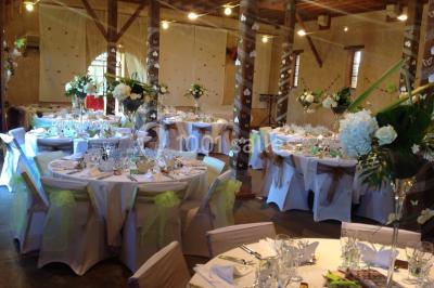 Intérieur d'une tente de réception avec tables rondes décorées, chaises en bois clair et lumière naturelle.