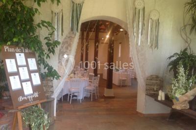 Intérieur d'une tente de réception avec tables rondes décorées, chaises en bois clair et lumière naturelle.