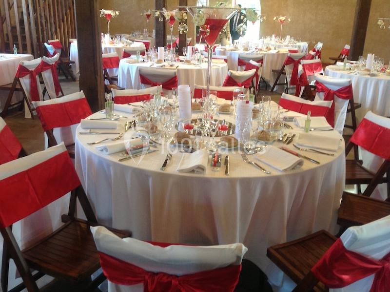 Salle de réception décorée avec des tables rondes, nappes blanches et chaises ornées de nœuds rouges.