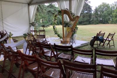 Intérieur d'une tente de réception avec tables rondes décorées, chaises en bois clair et lumière naturelle.