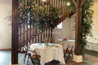 Intérieur d'une tente de réception avec tables rondes décorées, chaises en bois clair et lumière naturelle.