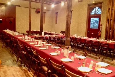 Intérieur d'une tente de réception avec tables rondes décorées, chaises en bois clair et lumière naturelle.