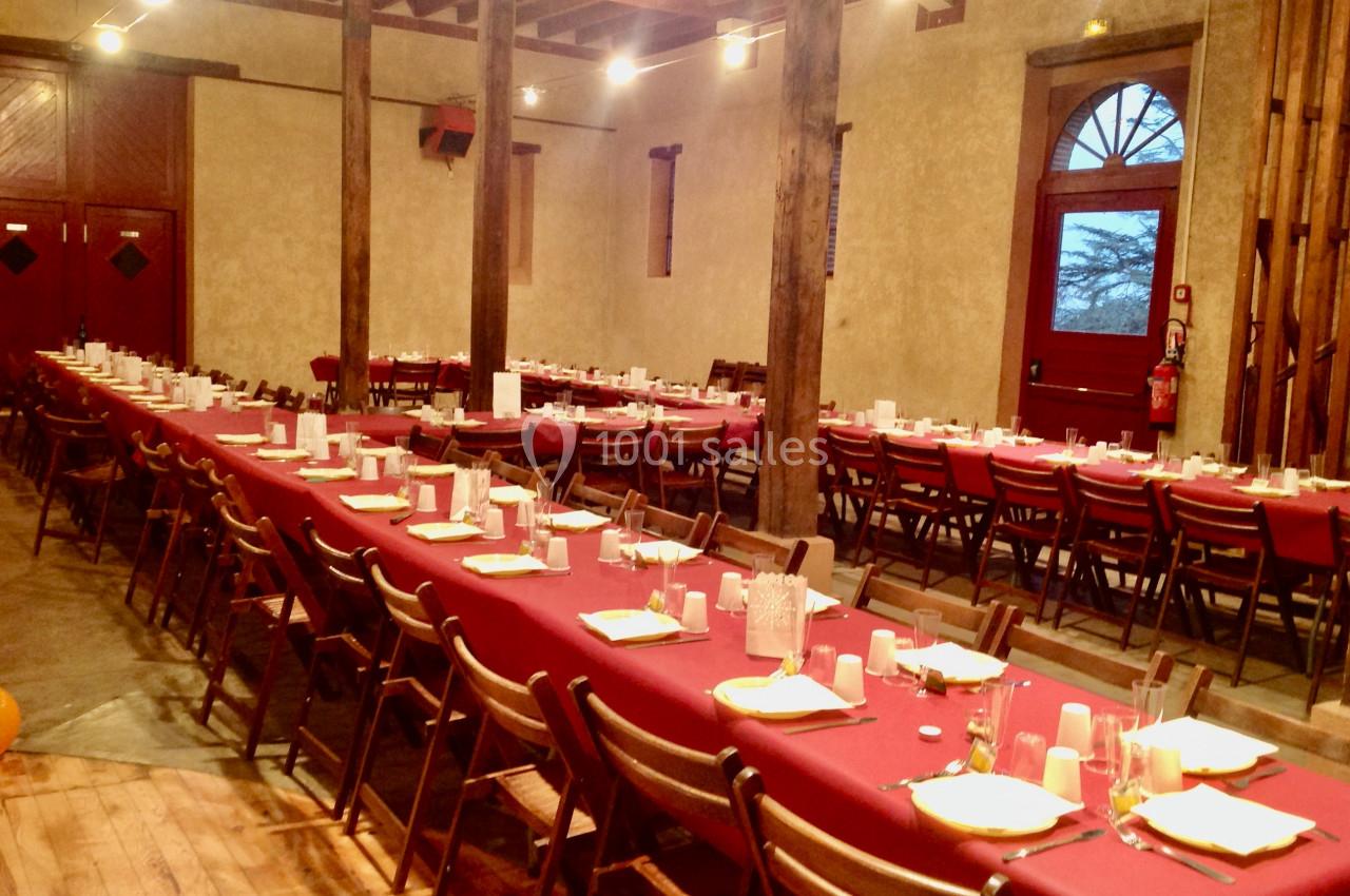 Salle de réception avec de longues tables dressées de nappes rouges, alignées avec des chaises en bois.